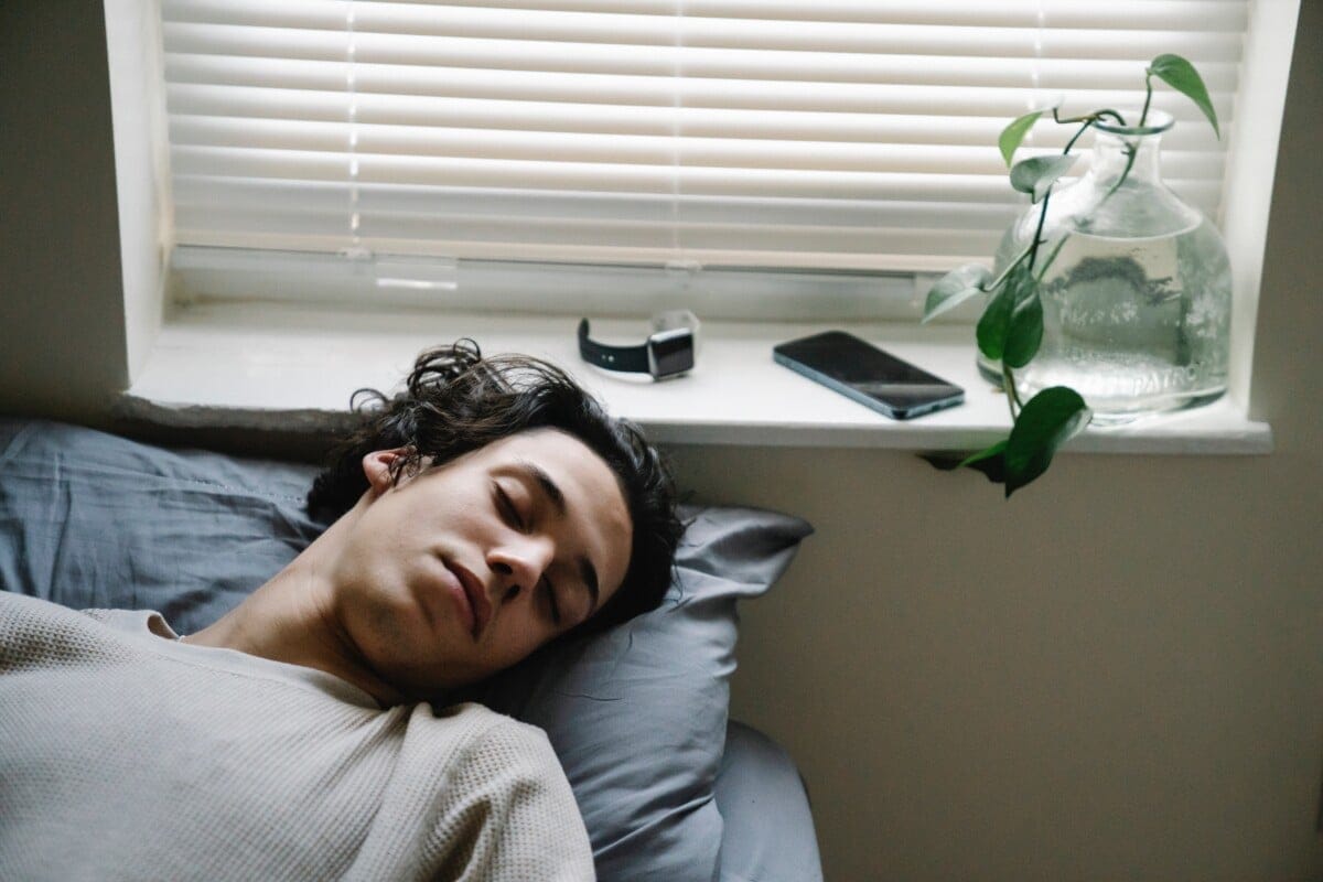 Teenager sleeping in bed during the day with smartphone and watch nearby