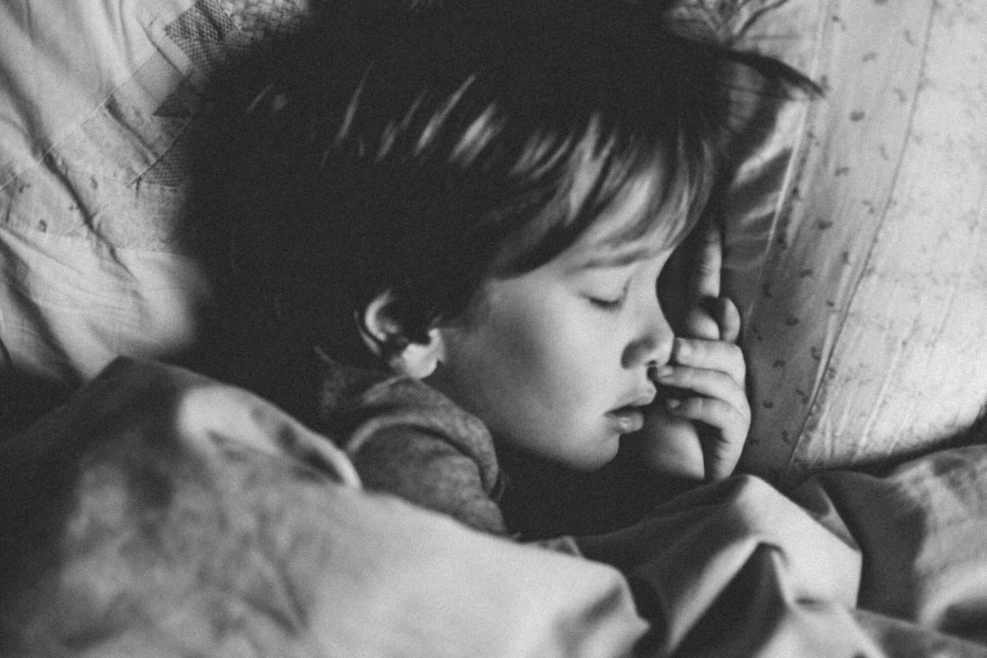 Black and white image of a child sleeping comfortably in bed