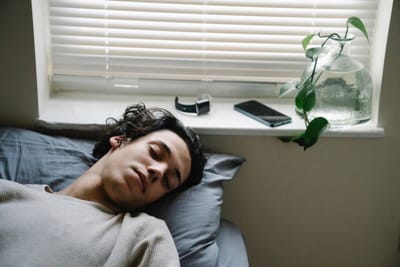 Teenager sleeping in bed during the day with smartphone and watch nearby